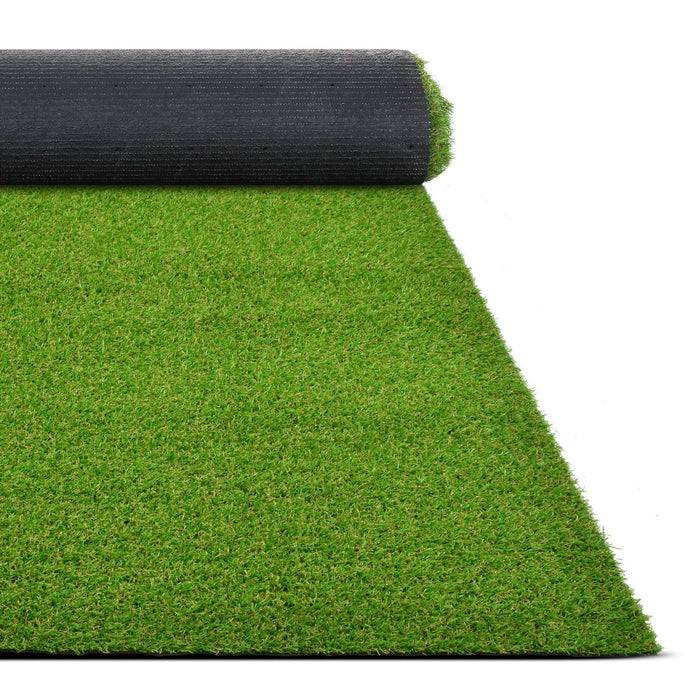 Eine Rolle aus künstlichem grünem Gras, teilweise auf weißem Hintergrund ausgerollt, zeigt lebendige Textur und Farbkontrast mit dunkler Rückseite.