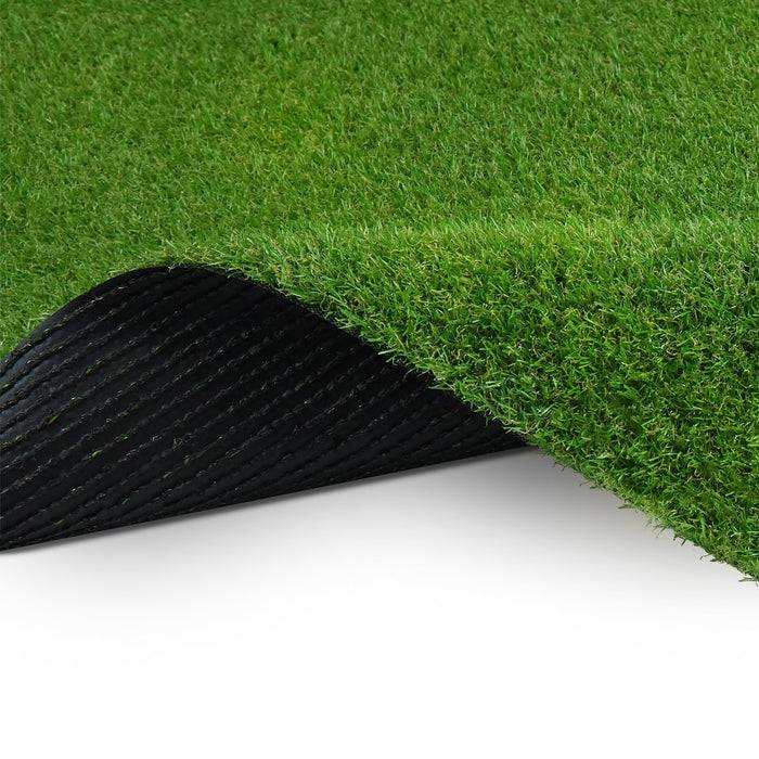 Eine Nahaufnahme einer künstlichen Grasmatte, die umgerollt ist und grüne Halme oben sowie eine strukturierte schwarze Rückseite unten zeigt.