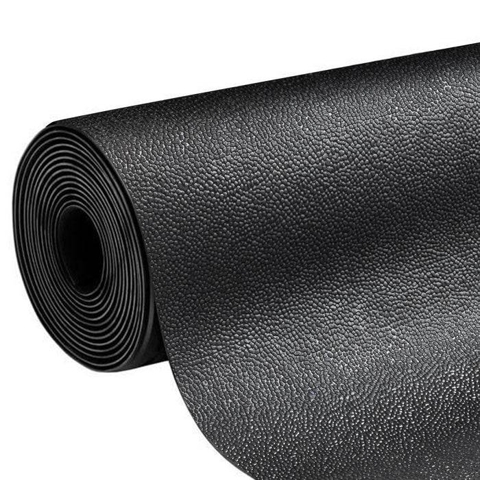 Eine schwarze, strukturierte Yogamatte, aufgerollt, aus einem Winkel betrachtet, wobei ihre Oberflächendetails und kompakte Form sichtbar sind.