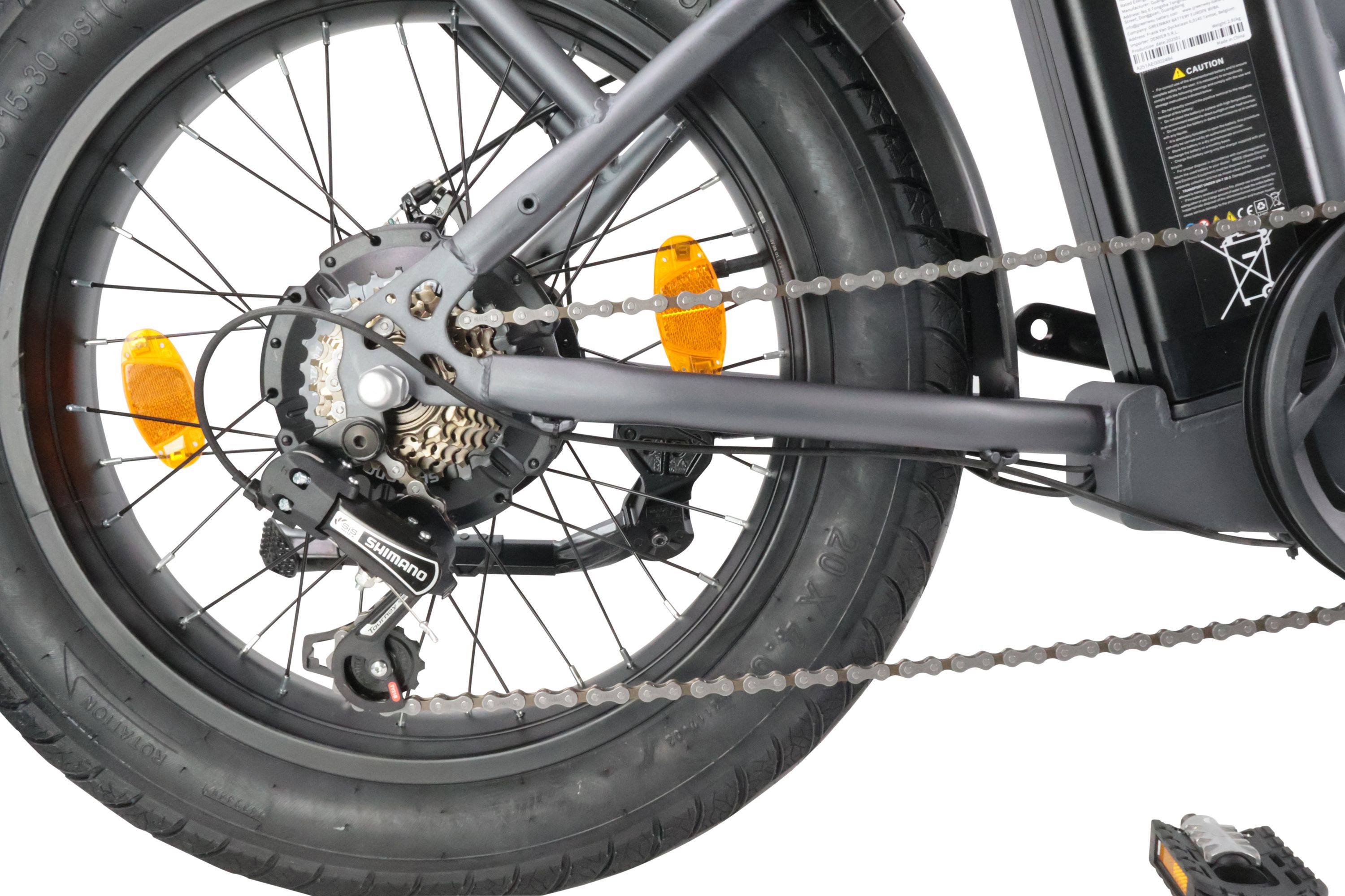 Hinterrad eines schwarzen Fahrrads mit Shimano-Schaltungssystem und gelbem Reflektor, was erhöhte Sichtbarkeit und Leistung anzeigt.