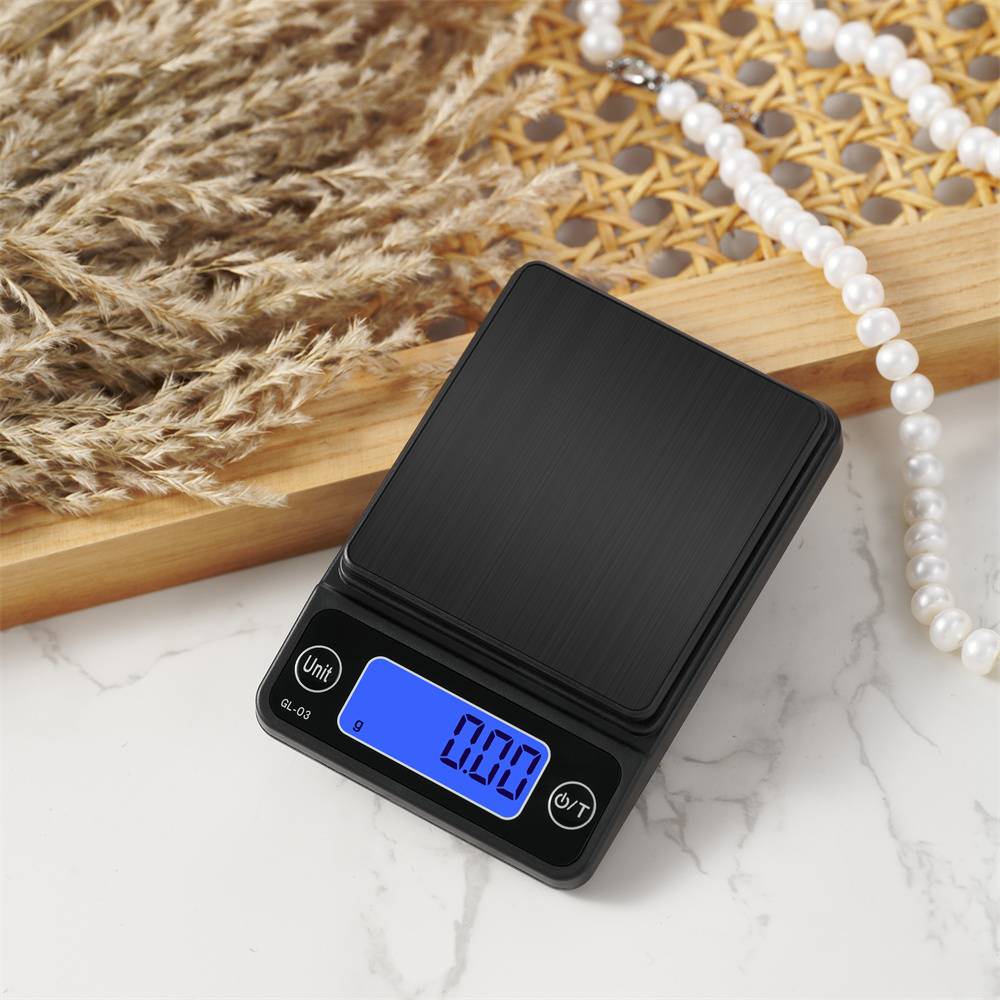 Eine digitale Waage zeigt 0,00 Gramm auf einem blauen Bildschirm an und steht auf einer weißen Marmoroberfläche neben einer Perlenkette und getrocknetem Gras.