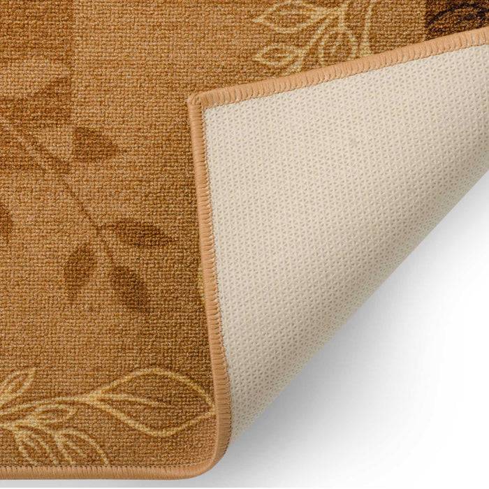 Ein beige und braun gemusterter Teppich mit Blattmustern, von der Unterseite gezeigt. Die Ecke des Teppichs ist umgeklappt und zeigt eine helle rutschfeste Unterseite.
