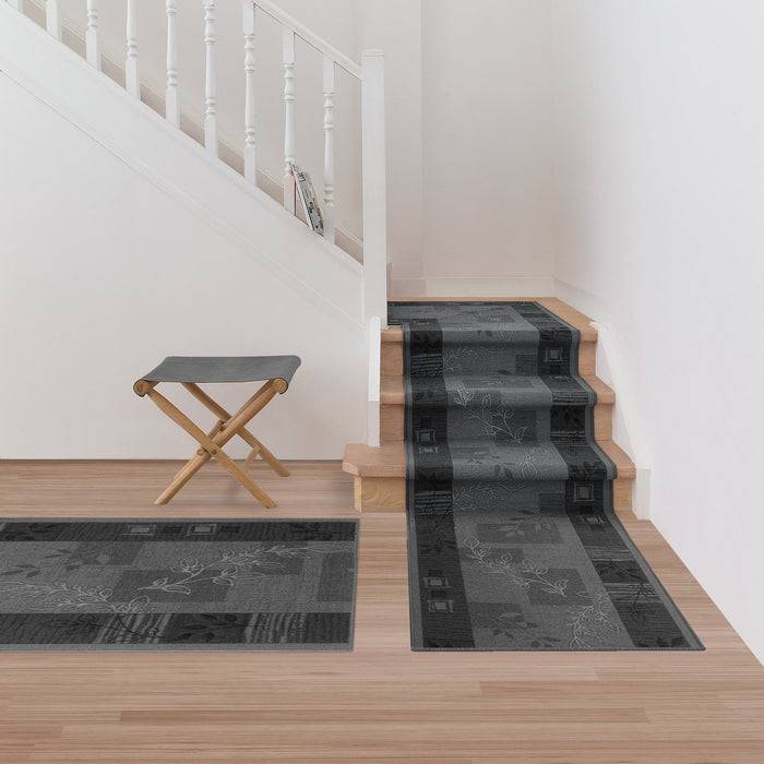 Ein grauer Treppen läufer und passende Teppiche mit geometrischen Mustern bedecken eine Treppe und den nahe gelegenen Boden. Ein kleiner Klapphocker steht neben der Treppe.