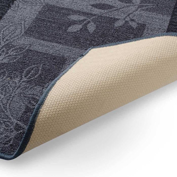 Eine Nahaufnahme einer Ecke eines blaugemusterten Teppichs, der umgefaltet ist und eine beige, strukturierte rutschfeste Unterseite zeigt.