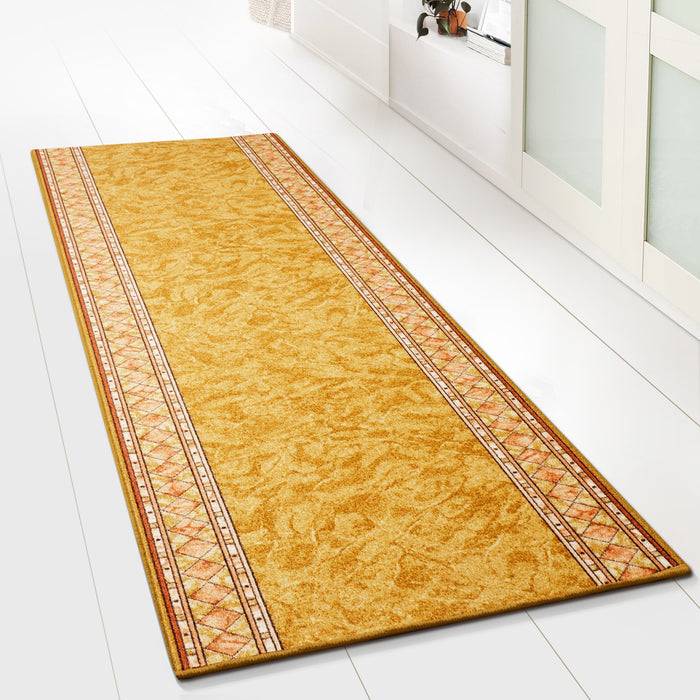 Ein beige und orange gemusterter Teppichläufer liegt auf einem weißen Fliesenboden, mit geometrischen Mustern eingefasst, in einem hellen, modernen Raum.