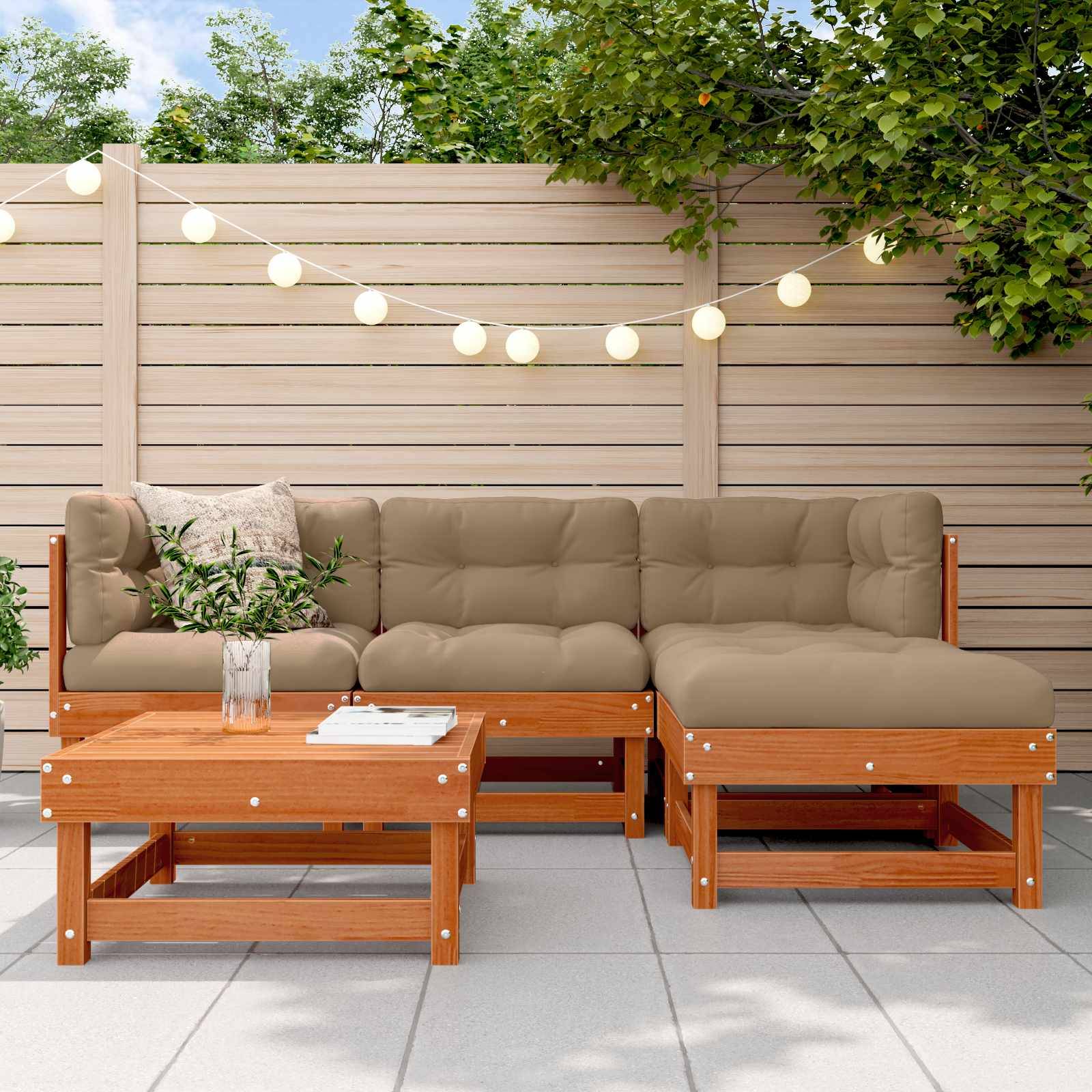 Outdoor-Terrasse mit einem Holz-Ecksofa und Couchtisch auf Fliesenboden, dekoriert mit Lichterketten und Grünpflanzen.