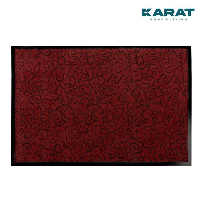 Eine rote Matte mit schwarzen abstrakten Wirbelmuster, mit schwarzem Rand umrandet, und dem Logo „Karat Home & Living