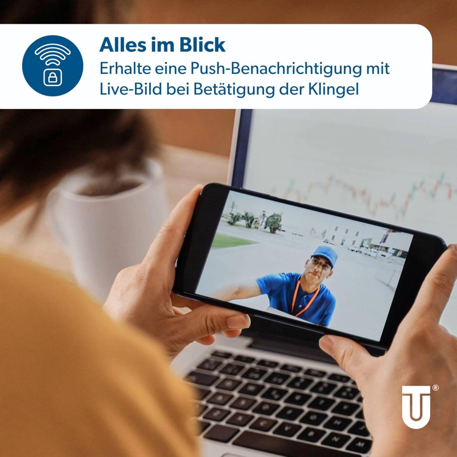 Person, die ein Telefon hält, auf dem ein Videoanruf mit einem Lieferperson angezeigt wird, mit einem Laptop im Hintergrund. Das Schild liest „Alles im Blick