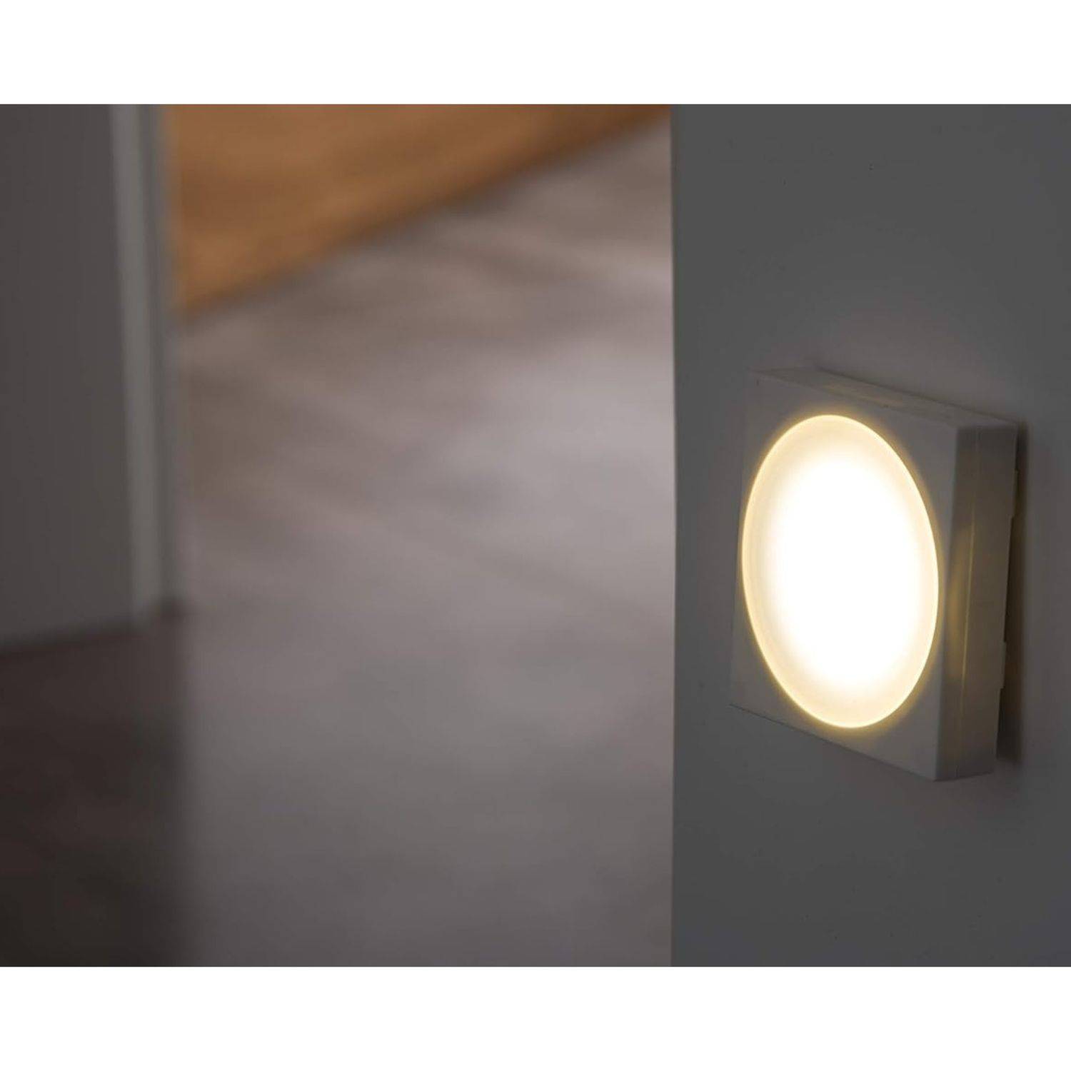 Ein kreisförmiges Nachtlicht wirft einen warmen Glanz auf eine Wand in einem schwach beleuchteten Zimmer und hebt den Eckbereich mit weicher Beleuchtung hervor.