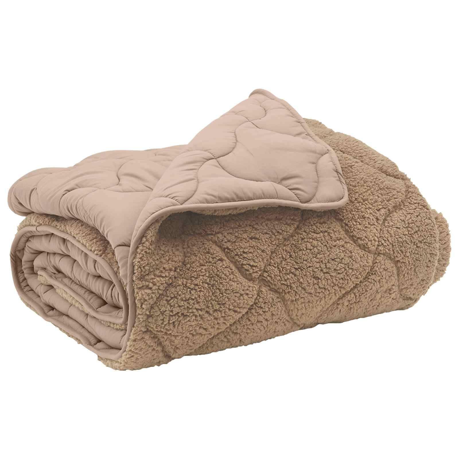 Eine gefaltete beige gesteppte Decke mit einem weichen, strukturierten Stoff auf einer Seite sichtbar, was Wärme und Komfort andeutet.