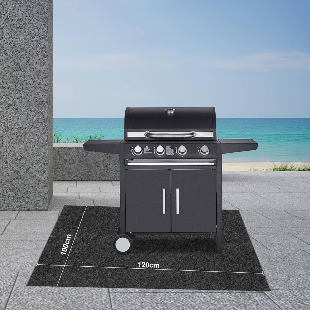 Ein schwarzer Gasgrill mit vier Brennern und zwei Seitentischen steht auf einer strukturierten Matte mit den Maßen 120cm x 100cm in der Nähe einer Terrasse am Meer.