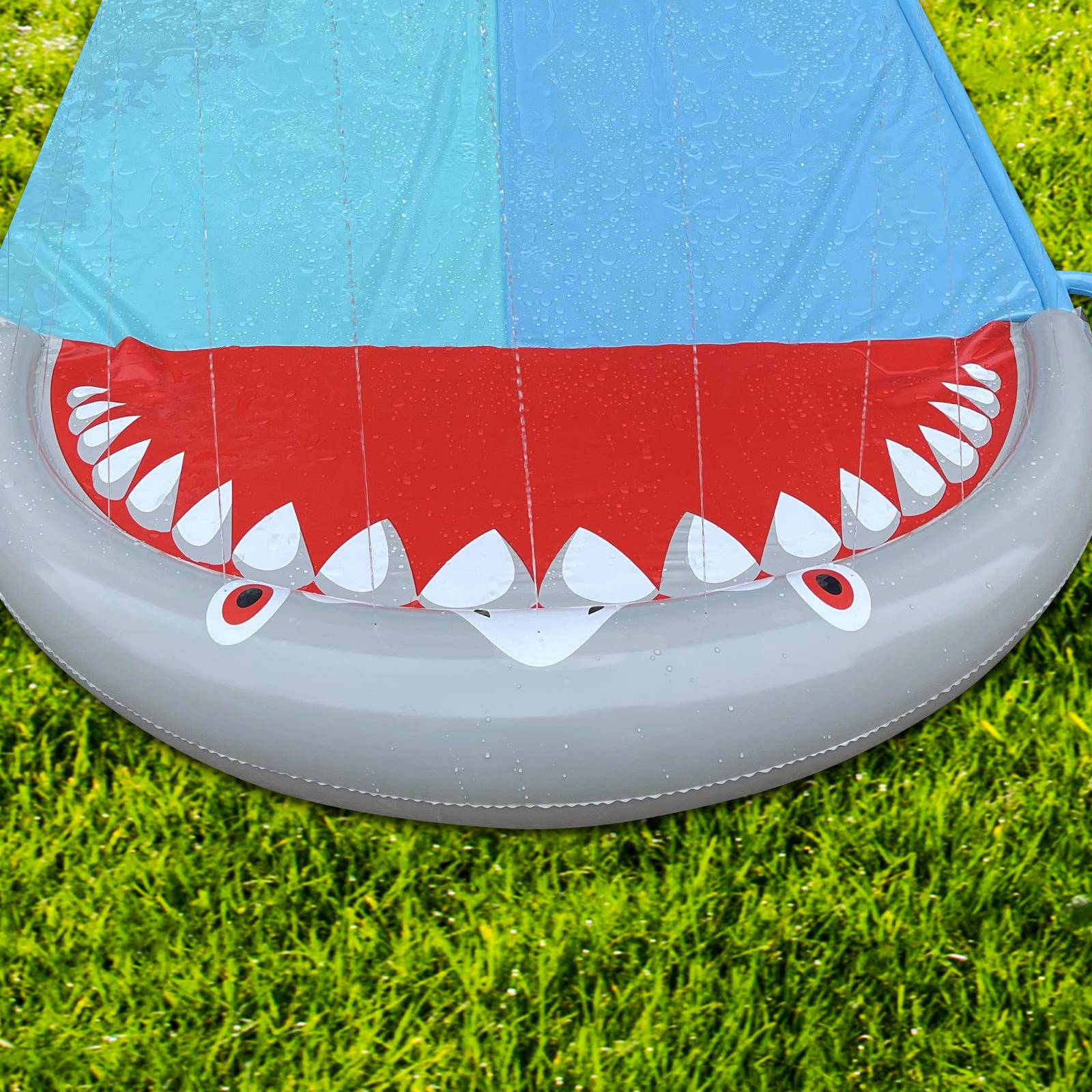 Ein aufblasbares rundes Spielzeug, das einem offenen Hai-Maul mit sichtbaren Zähnen ähnelt, auf grünem Gras platziert. Es hat blaue und rote Abschnitte.