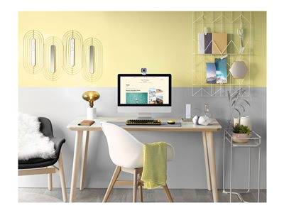 Ein minimalistisches Heimbüro mit einem Schreibtisch, Computer und Stuhl. Die Einrichtung umfasst eine kleine Lampe, Wandkunst und Regale mit Büchern und Pflanzen.