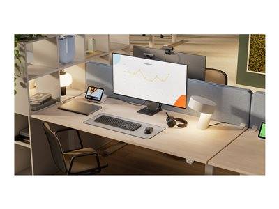 Ein modernes Bürotischaufbau mit einem großen Monitor, der ein Liniendiagramm anzeigt, Laptop, Tastatur und Kopfhörer. Warme Umgebungsbeleuchtung.