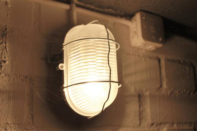 Ein Wandleuchten-Fixture im Vintage-Stil mit geriffeltem Glasschirm und Metallkäfig auf einer strukturierten Wand montiert, die ein warmes Licht ausstrahlt.
