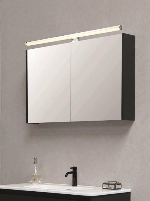 Ein an der Wand montierter Badezimmerschrank mit verspiegelten Türen und einer Oberleuchte. Eine Flasche und ein Wasserhahn sind unter dem Schrank sichtbar.