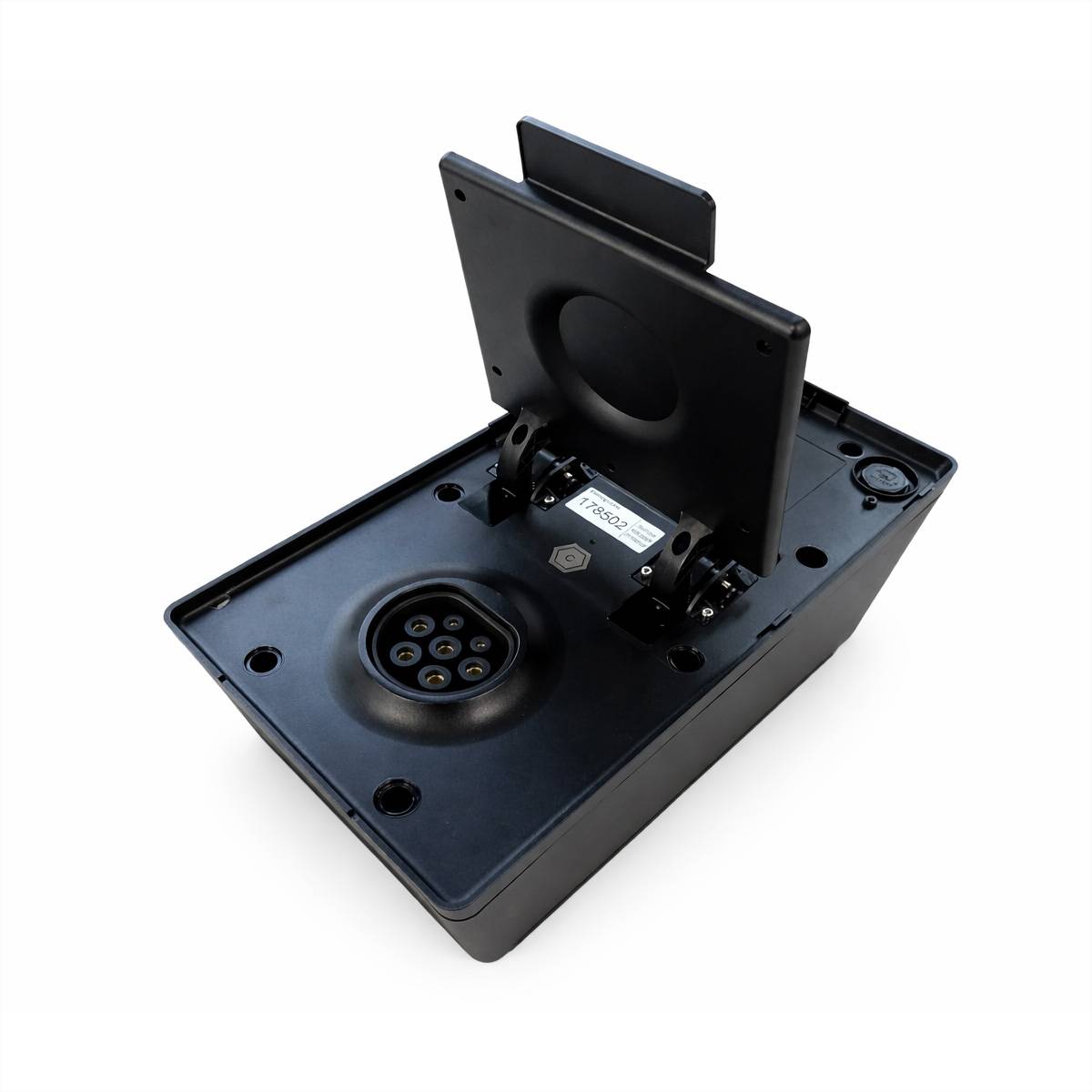 Ein schwarzer Fahrzeugladestecker mit aufklappbarem Deckel, der mehrere Stiftlöcher für die elektrische Verbindung zeigt, ruhend auf einer ebenen Fläche.