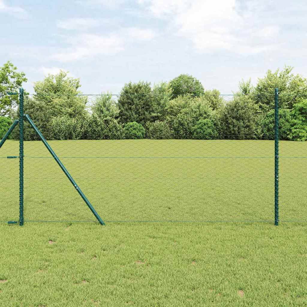 Ein grüner Zaun steht in einem grasbewachsenen Feld mit einem Hintergrund aus dichten, belaubten Bäumen unter einem bewölkten Himmel.
