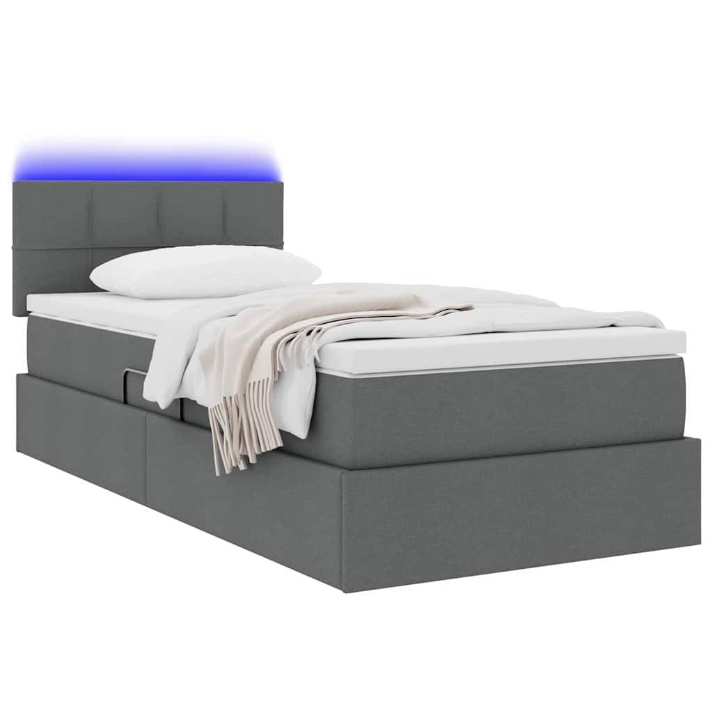 Ein graues Polsterbett mit Kopfteil und blauer LED-Beleuchtung. Das Bett ist sorgfältig mit einem weißen Laken und einer beigen Decke gemacht.