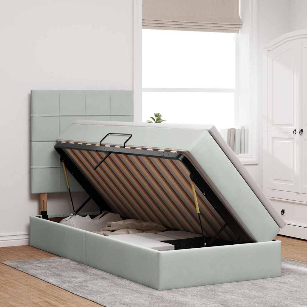Ein hellgraues Polsterbett mit hochgeklappter Oberseite, das Stauraum darunter freigibt. Es steht in einem Schlafzimmer in der Nähe eines Fensters.