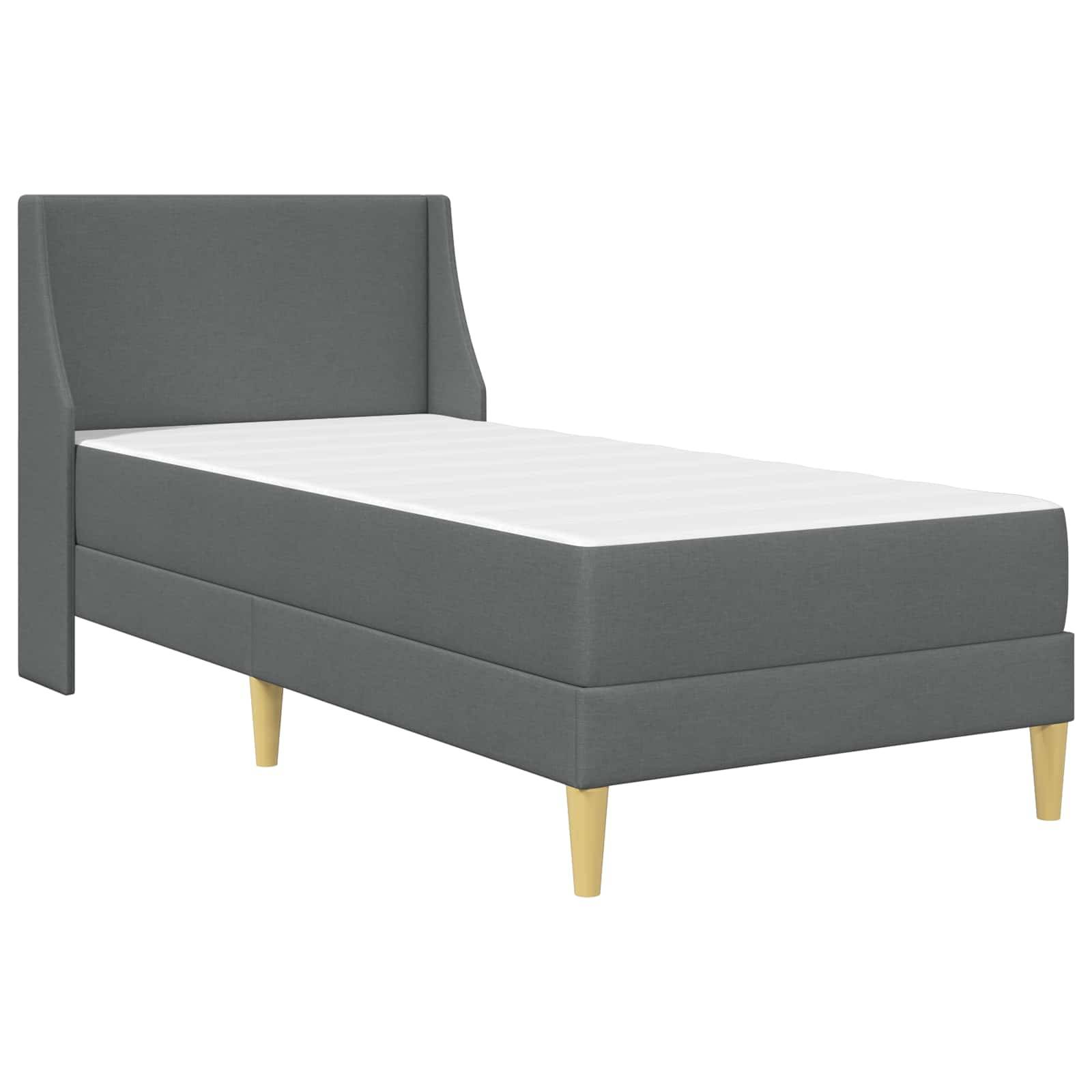 Ein graues Einzelbett mit geometrischem Kopfteil und hellen Holzbeinen, in minimalistischem Stil eingerichtet.
