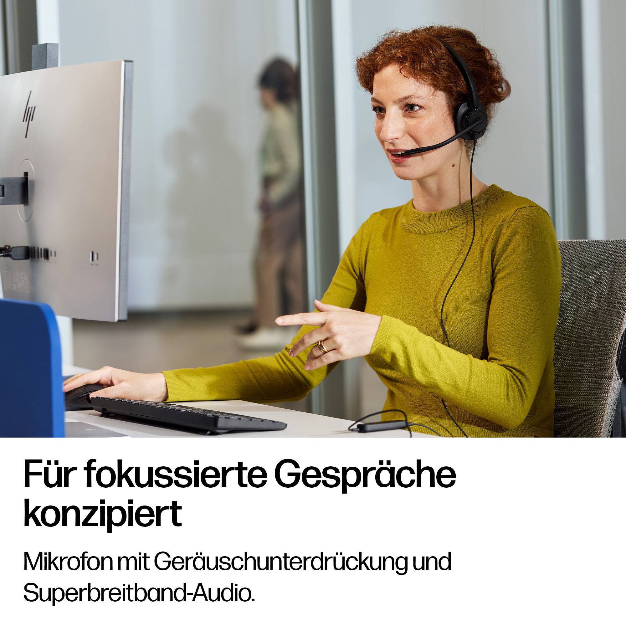 Frau mit Kopfhörer arbeitet an einem Schreibtisch neben einem Monitor; der deutsche Text lautet „Für fokussierte Gespräche konzipiert