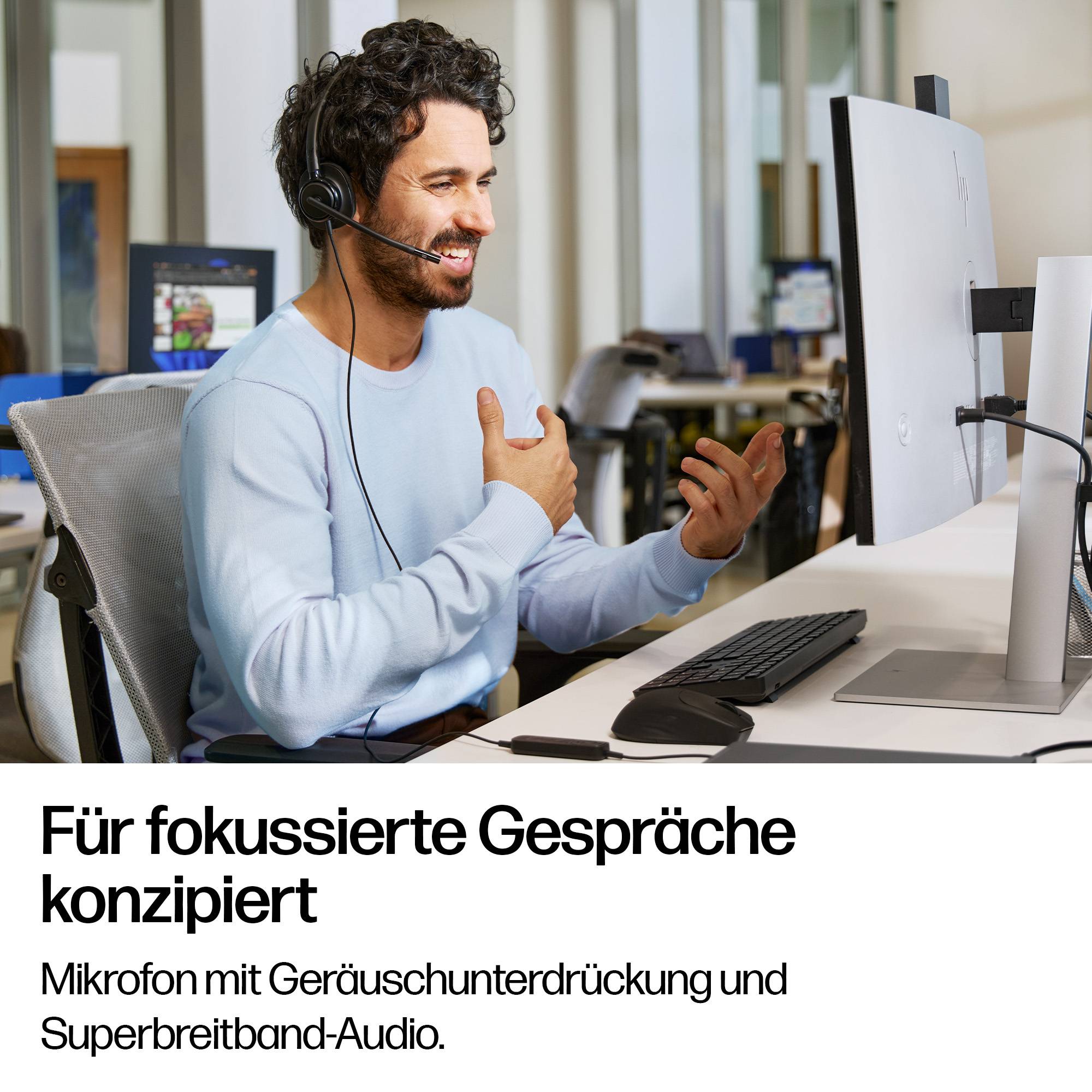 Ein Mann mit Headset spricht an einem Schreibtisch mit Monitor und Tastatur; deutscher Text liest 