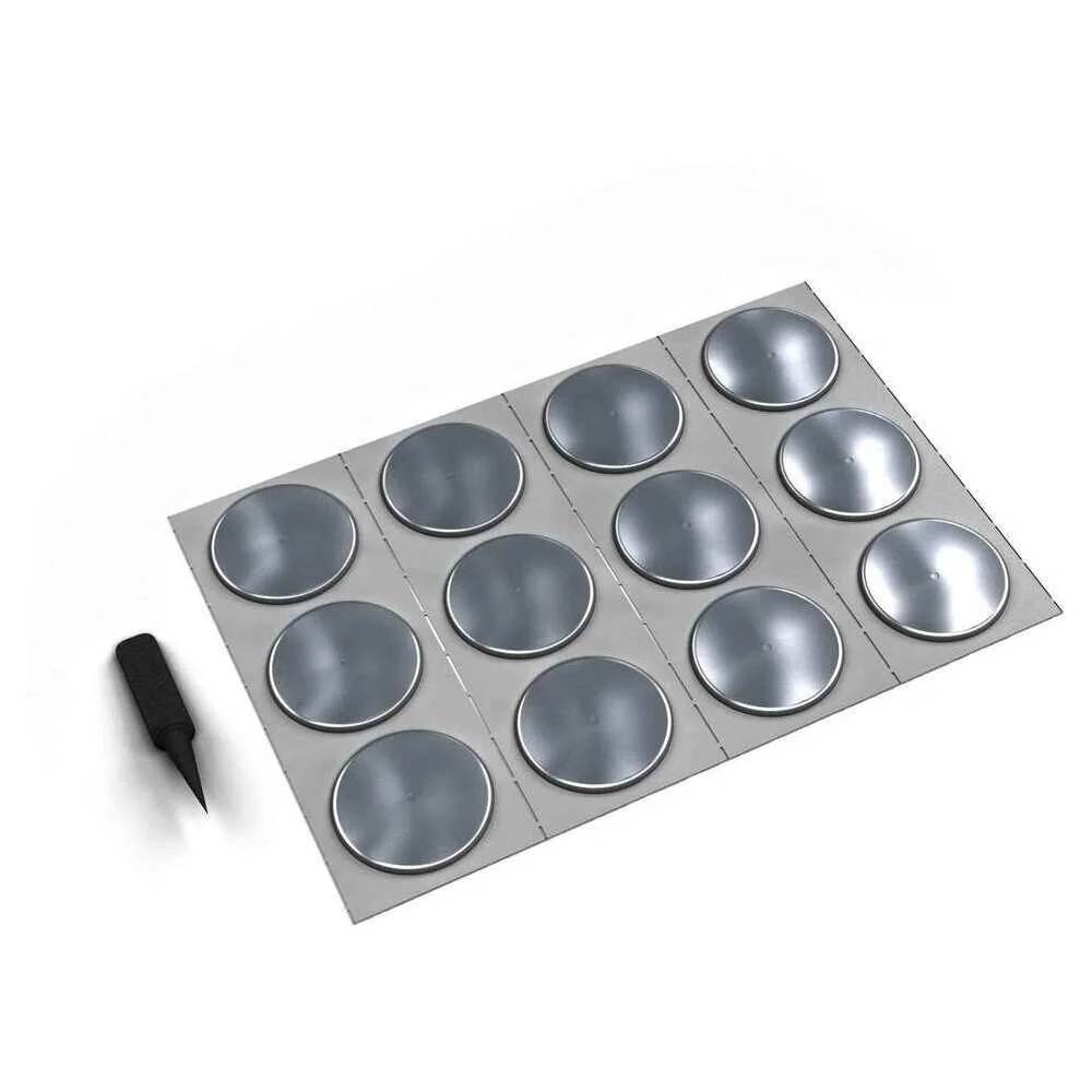 Ein graues Blatt mit 12 kreisförmigen metallischen Scheiben in einer Gitteranordnung, daneben ein kleines schwarzes Auswahlwerkzeug.