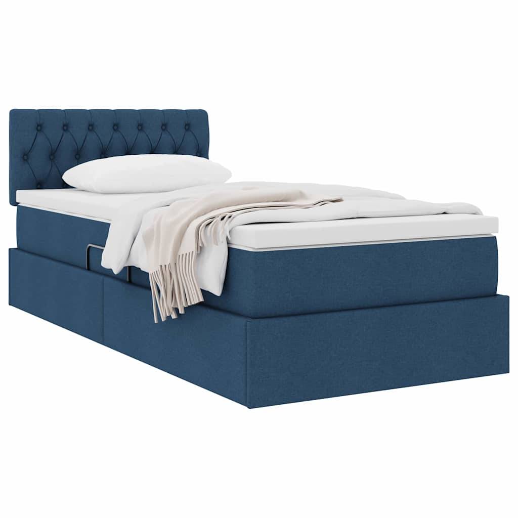Blaues Polsterbett mit gestepptem Kopfteil, weißen Kissen und Laken sowie einer beigefarbenen Wurfdecke. Das Bett hat Schubladen zur Aufbewahrung darunter.