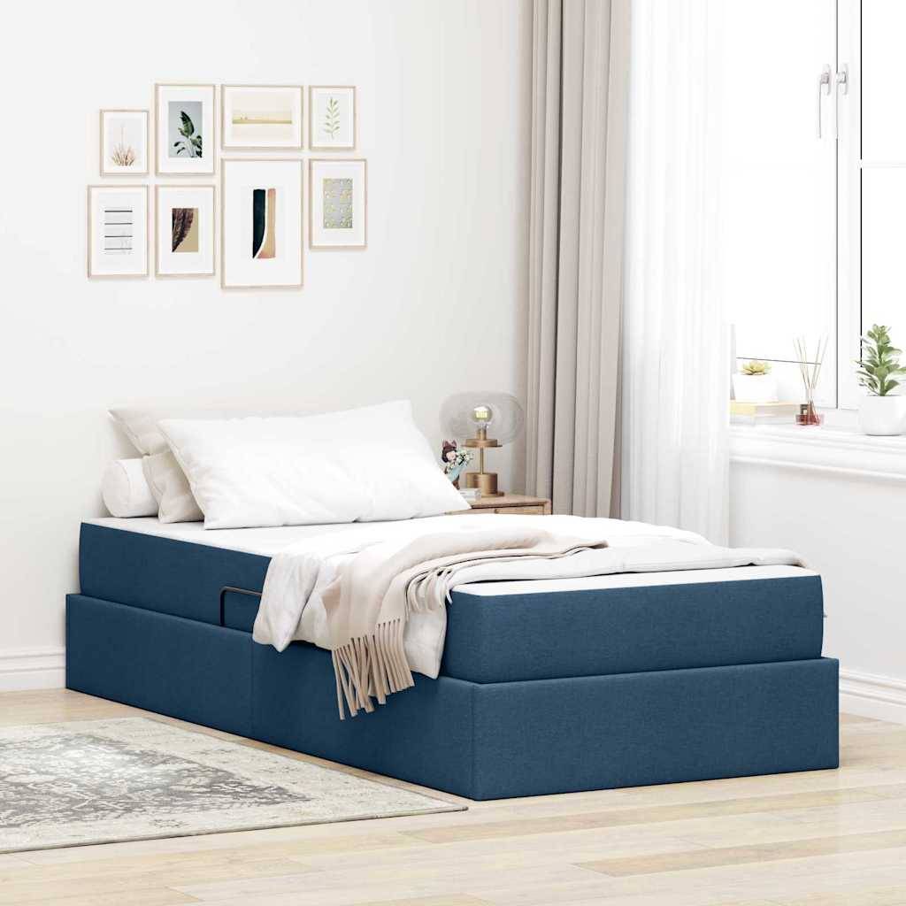 Ein modernes Schlafzimmer mit einem blauen Stauraumbett, weißer Bettwäsche und einer beigefarbenen Wurfdecke. Eine Wand zeigt gerahmte Kunstwerke, und Vorhänge ermöglichen weiches natürliches Licht.