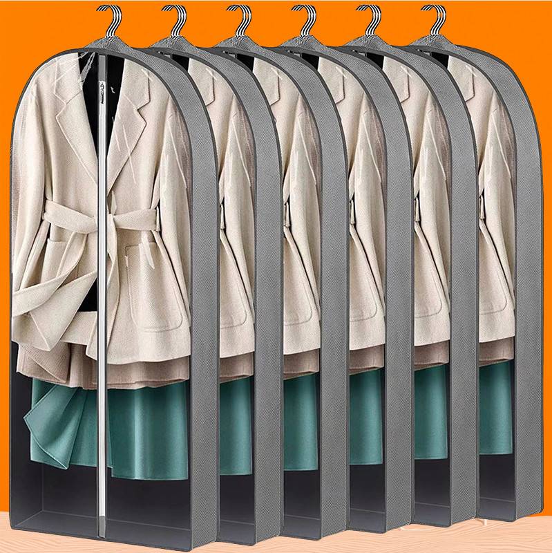 Sechs beige Mäntel in Kleidersäcken aufgereiht, hängen an Haken vor orangefarbenem Hintergrund.