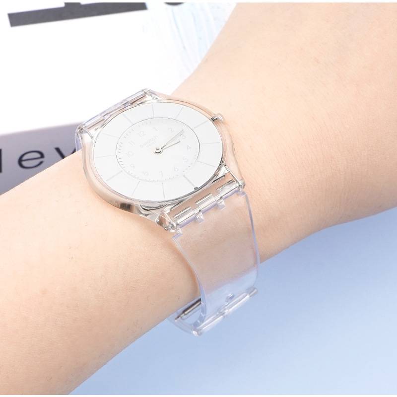 Transparente Armbanduhr mit minimalistischem Design, mit durchsichtigem Armband und weißem Zifferblatt, getragen am Handgelenk einer Person.