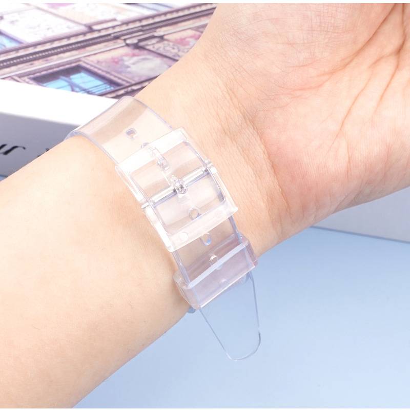 Eine Hand mit einem durchsichtigen Kunststoffuhrenarmband, das ihre verstellbaren Löcher und das durchscheinende Material gegen eine hellblaue Oberfläche zeigt.