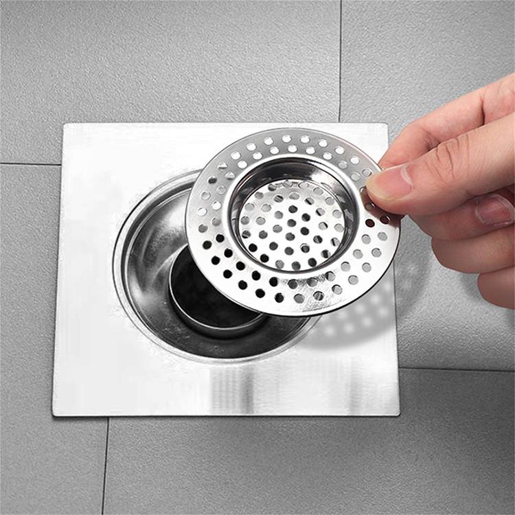 Eine Hand legt einen runden Metallablaufdeckel mit Löchern über einen quadratischen Spülbechenablauf und zeigt so eine Methode zur Vermeidung von Verstopfungen.
