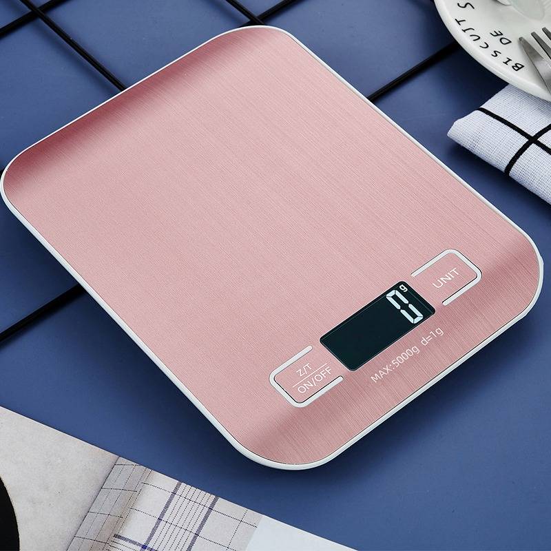 Eine digitale Küchenwaage mit einer rosegoldfarbenen Wiegeplattform und einem blauen Display, das „0 g" anzeigt. Sie steht auf einer gefliesten Arbeitsplatte.