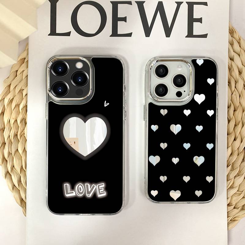 Zwei Handyhüllen auf einer gewebten Matte. Die linke Hülle ist schwarz mit einer Herzausschnitt und dem Text "LOVE"". Die rechte Hülle ist schwarz mit Herzmustern.