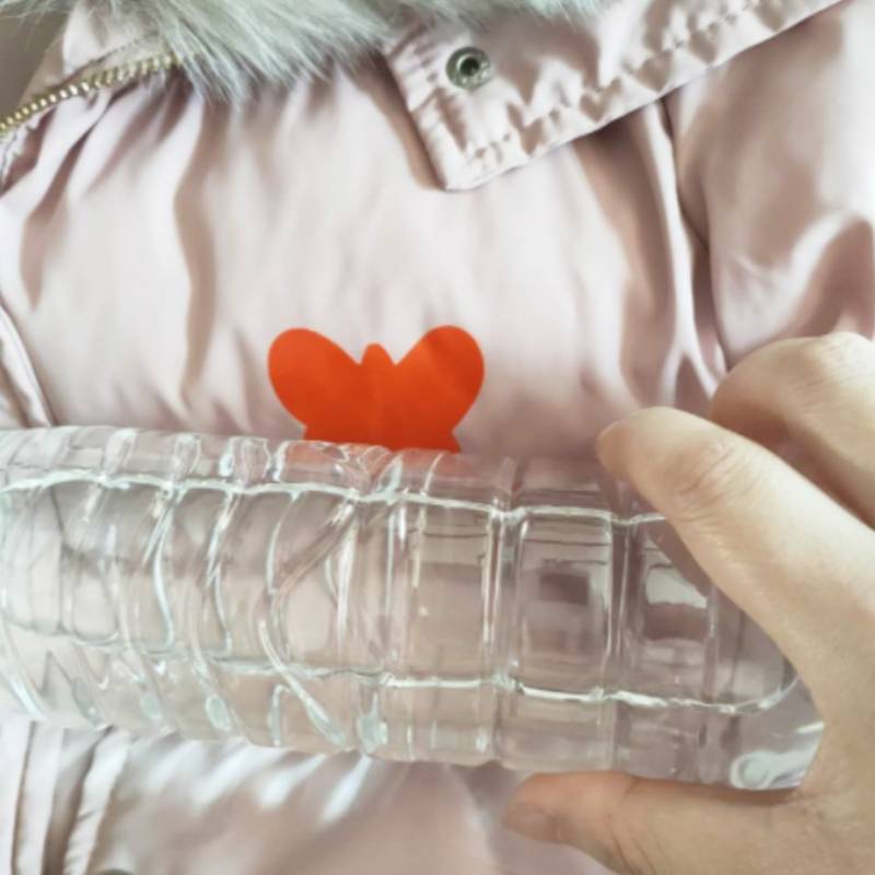 Eine Person hält eine durchsichtige Kunststoff-Wasserflasche in ihrer rechten Hand und trägt eine hellrosa Jacke mit einem roten Herzdesign auf der Brust.