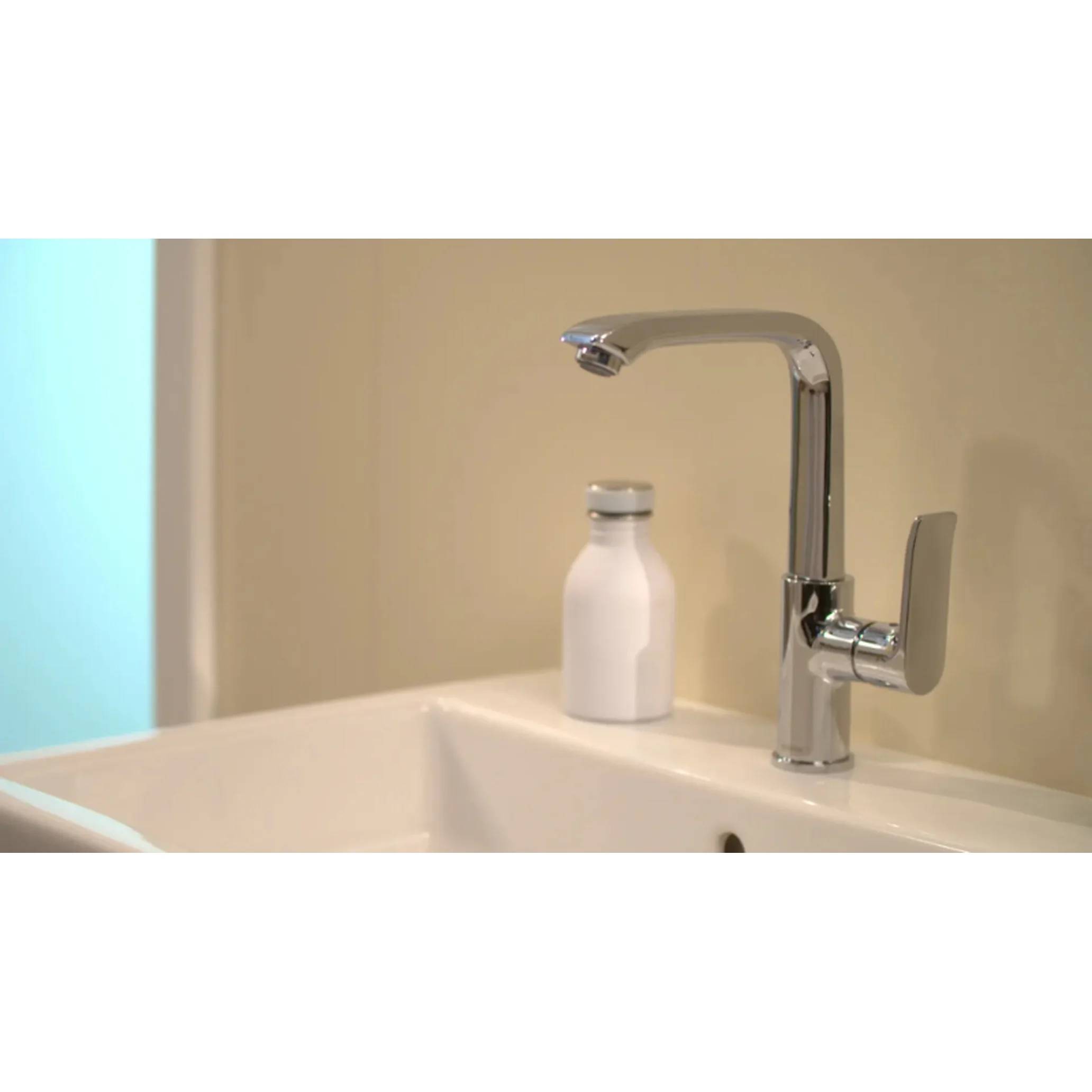 Chromwasserhahn im Badezimmer über einem weißen Waschbecken, mit einer kleinen weißen Flasche dahinter an einer beigefarbenen Wand.