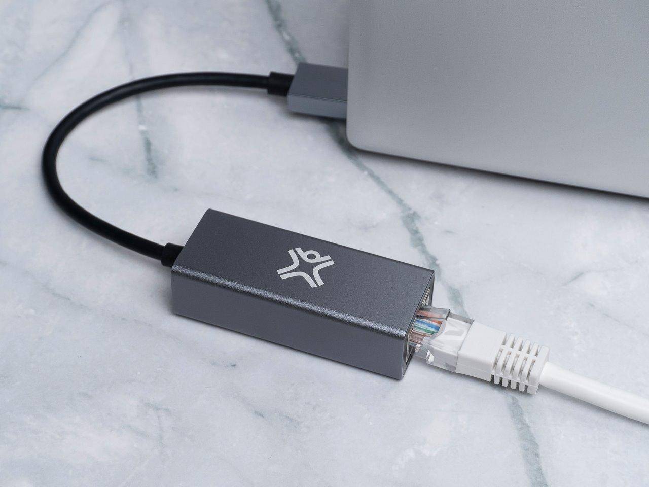 Ein Ethernet-Kabel verbindet sich mit einem silbernen Netzwerkadapter auf einer Marmoroberfläche und erweitert die Netzwerkfähigkeit auf ein nahegelegenes Gerät.