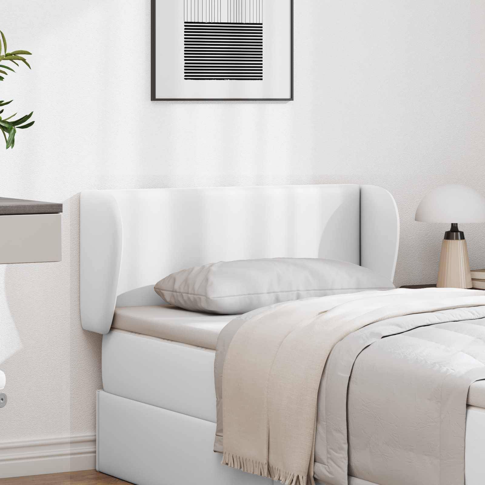 Ein minimalistisches Schlafzimmer mit einem weißen Bett, grauem Kissen und beigefarbener Decke. Ein Nachttisch mit einer Lampe befindet sich auf der rechten Seite. Moderne Kunstwerke hängen darüber.