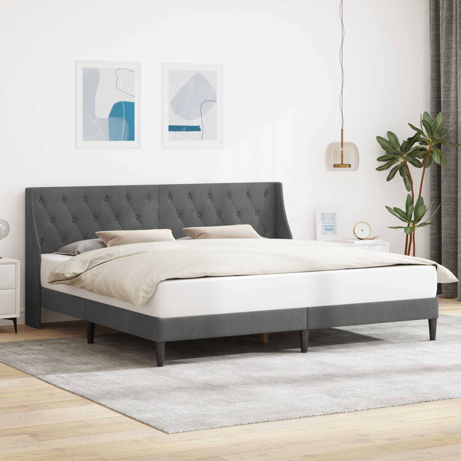 Ein modernes Schlafzimmer mit einem grau gepolsterten Bett, beigefarbener Bettwäsche, zwei abstrakten Kunstwerken an der Wand, einer hängenden Leuchte und einer Topfpflanze.