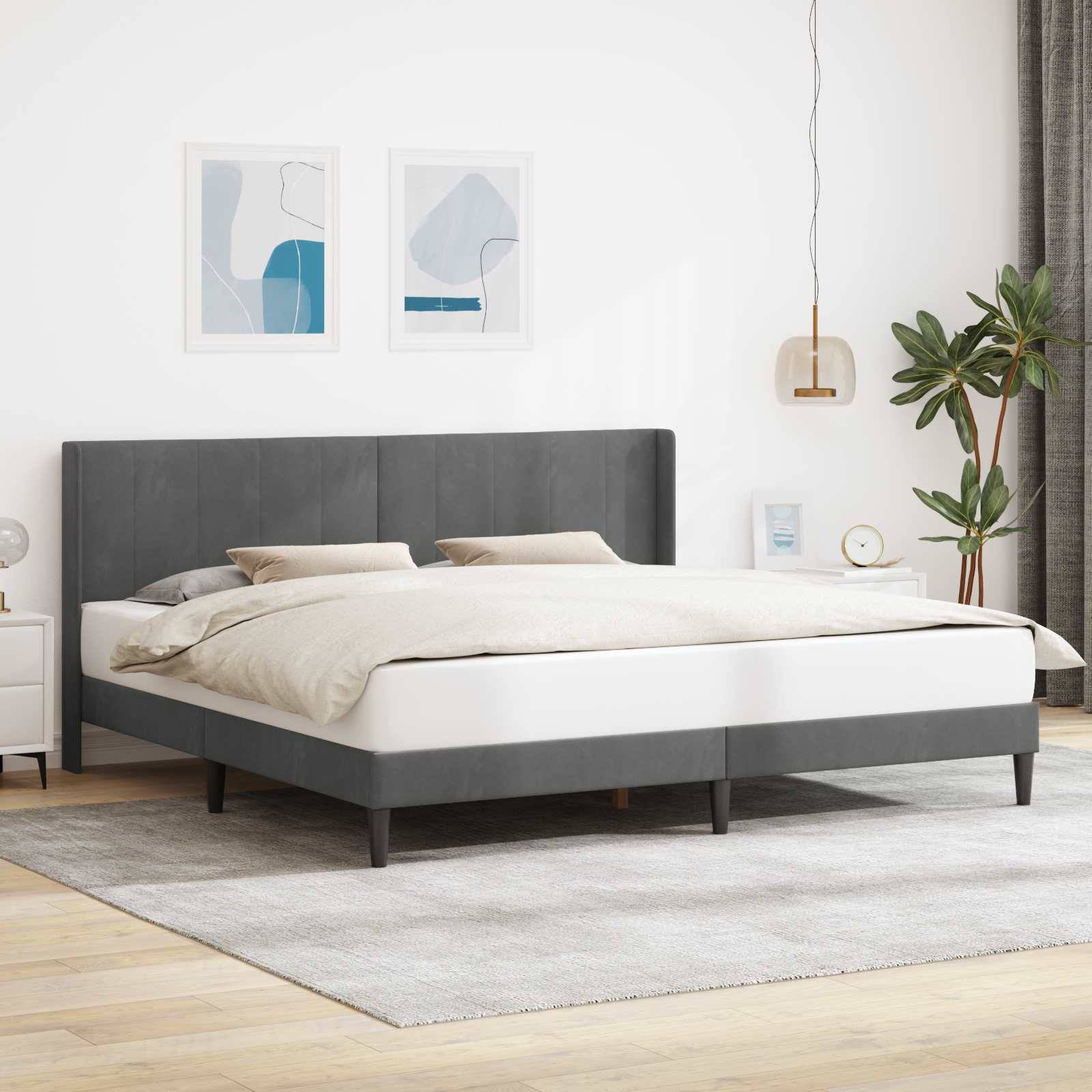 Ein modernes Schlafzimmer zeigt ein großes graues Bett mit getuftertem Kopfteil. Zwei minimalistische Kunstwerke hängen über dem Bett. Ein Nachttisch hält eine Lampe und eine Pflanze.