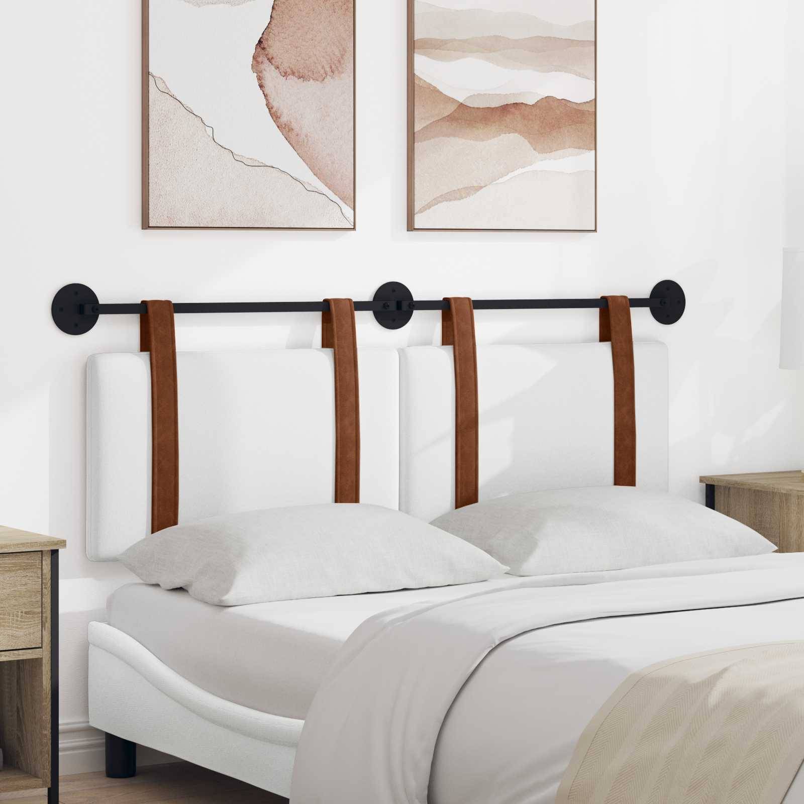 Ein modernes Schlafzimmer zeigt ein weißes Bett mit braunen Akzentriemen, das von Nachttischen flankiert wird. Zwei abstrakte Kunstwerke hängen über dem Bett.