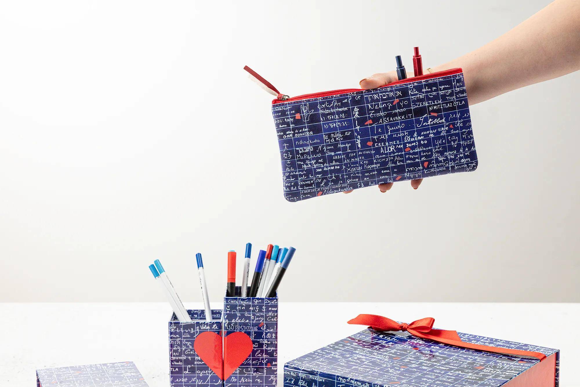 Eine Hand hält ein Stiftetui mit Marinebluem-Muster mit Stiften; passende Schreibtischorganizer und eine Geschenkbox sitzen darunter auf weißem Hintergrund.