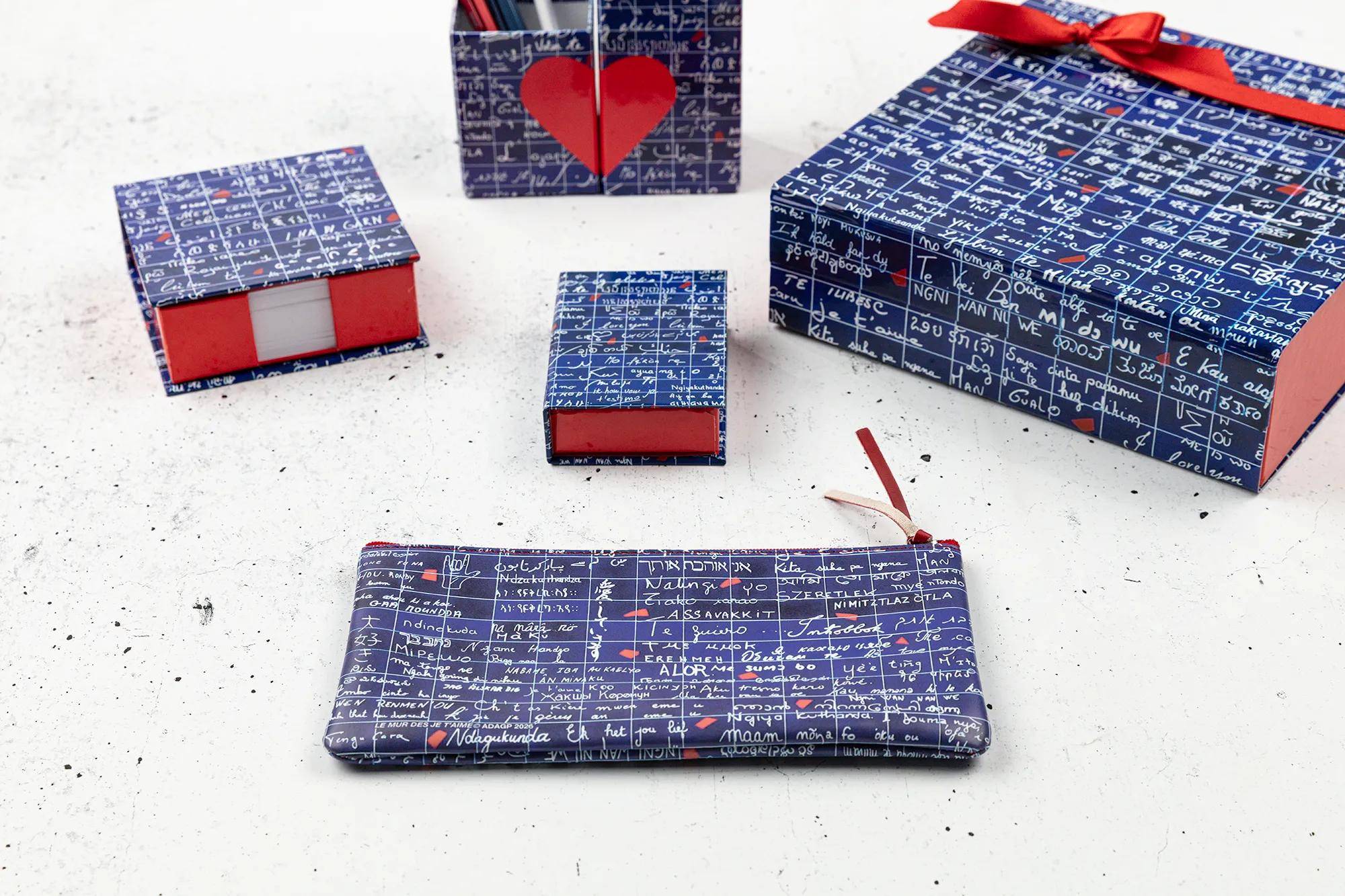 Geschenkboxen und eine passende Geldbörse in blauem Musterpapier eingewickelt, auf einer weißen Oberfläche mit roten Schleifenakzenten angeordnet.