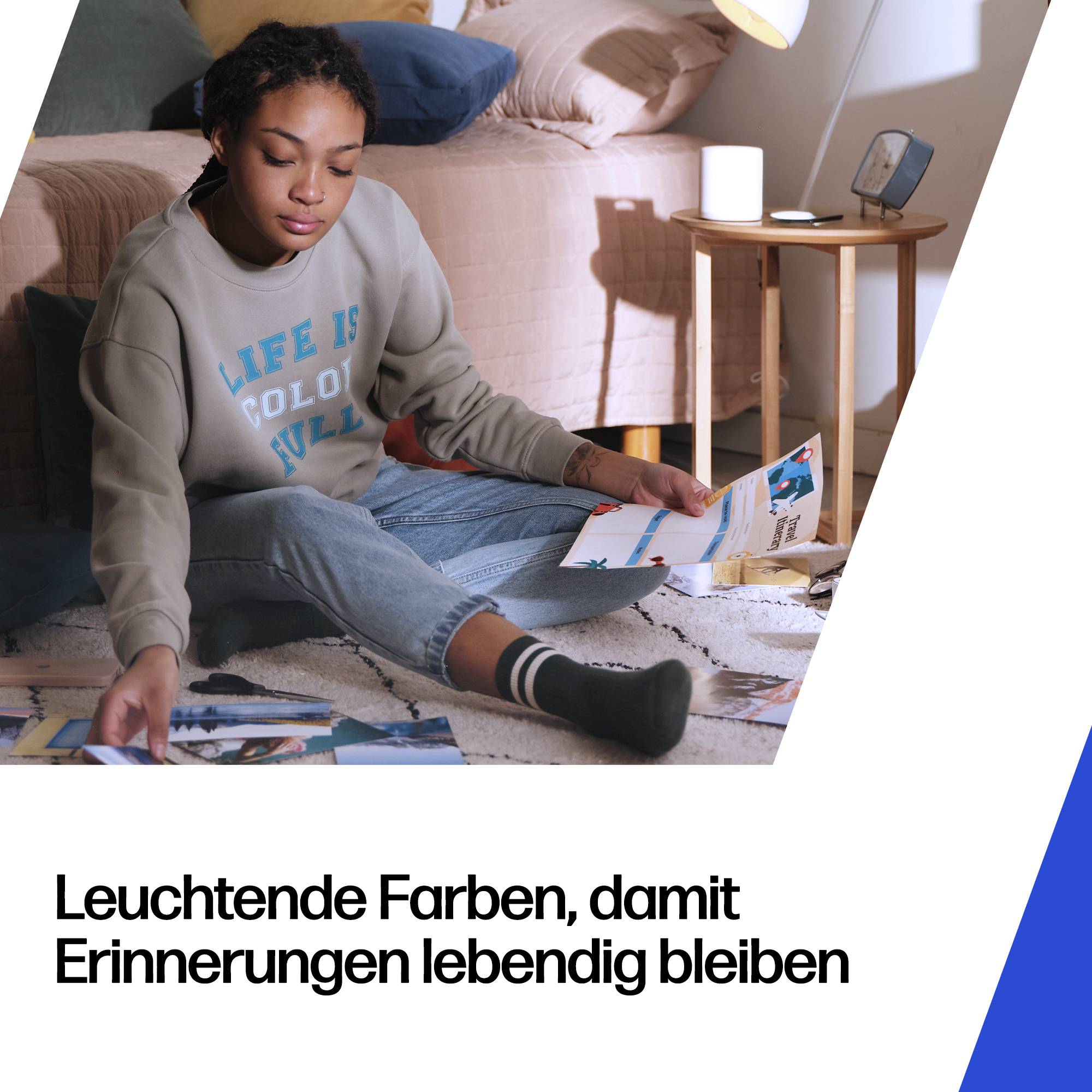 Junge Frau sitzt auf dem Boden in einem Schlafzimmer und sortiert gedruckte Fotos; deutscher Text lautet „Leuchtende Farben, damit Erinnerungen lebendig bleiben