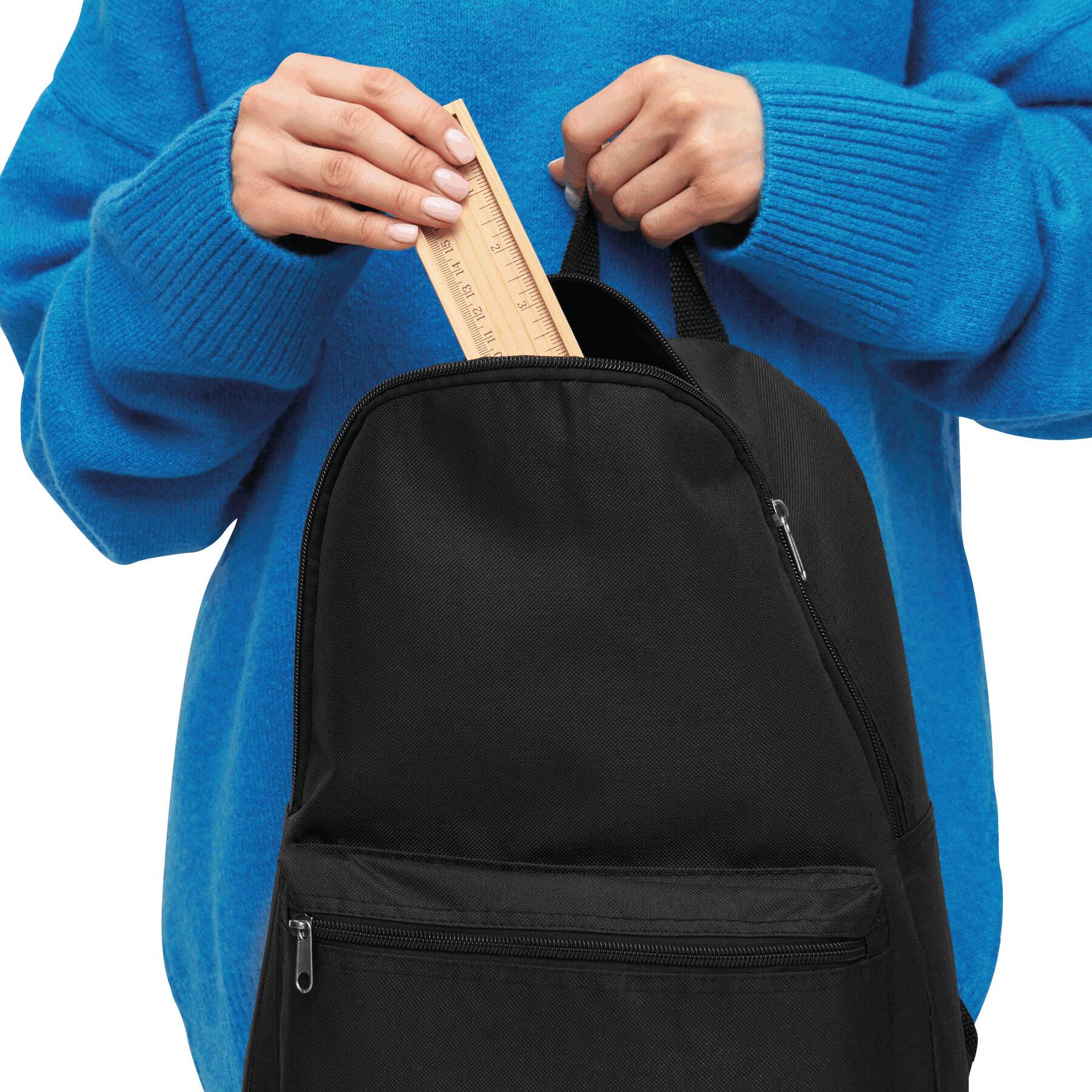 Eine Person, die einen blauen Pullover trägt, steckt ein Lineal aus Holz in einen schwarzen Rucksack.