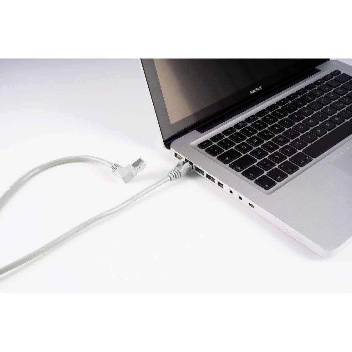 Ein teilweise geöffneter Laptop mit einem Stromkabel, das in seine Seite eingesteckt ist, auf einer weißen Oberfläche platziert.