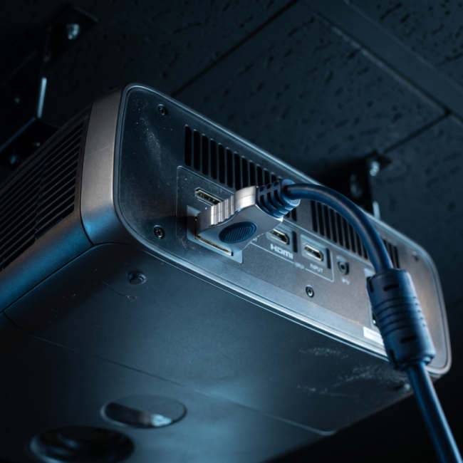 Nahaufnahme der hinteren Anschlüsse eines Beamers mit einem eingesteckten HDMI-Kabel, das Videoeingänge zeigt.