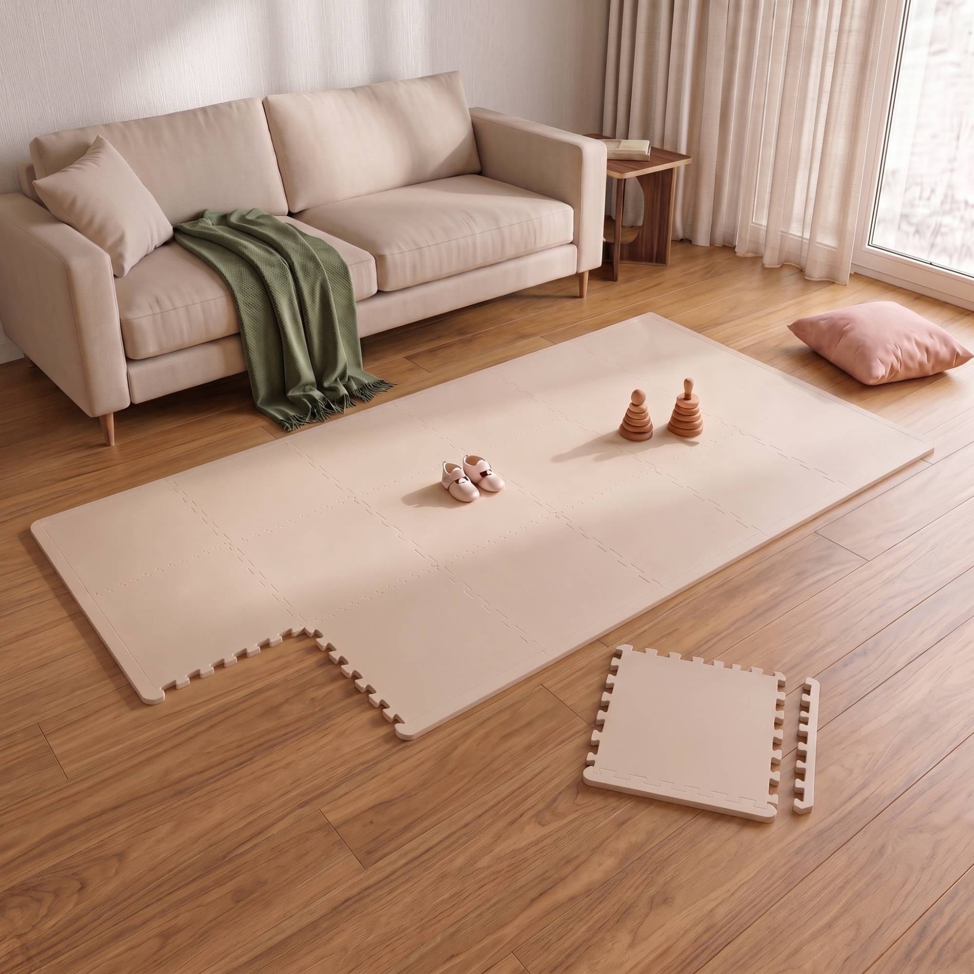 Helles Wohnzimmer mit beigem Sofa, Holzboden, Schaumstoff-Spielmatte, kleinen Spielzeugen und einem Kissen am Fenster.